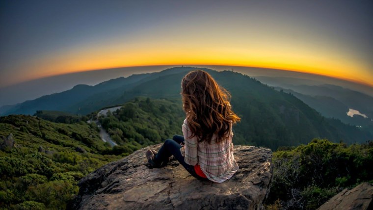 Девушка на закате на горе сидит спиной